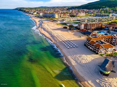 Langer Sandstrand mit Hotels, Liegestühlen und grün-blauem Meer an sonnigem Küstenhang.