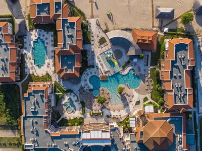 Luftaufnahme eines großen Resorts mit Poolanlagen, Sonnenschirmen, Wegen und mehreren Gebäuden.
