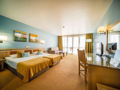 Geräumiges Hotelzimmer mit zwei Betten, Schreibtisch, Stühlen und großem Fenster mit Vorhängen.