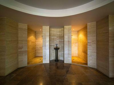 Eleganter Hotelflur mit hellen, verputzten Wänden, zentraler Skulptur und warmem Licht.