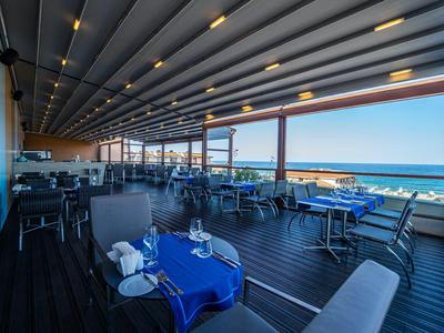 Offene Terrasse mit blau gedeckten Tischen und Meerblick in einem Hotelrestaurant.