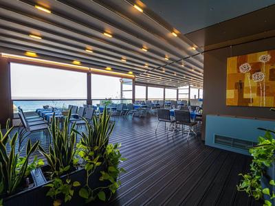 Offene Hotelterrasse mit Meerblick, Holzfußboden und modernen Pflanzen.