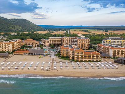 Mehrere Hotelgebäude mit einem Sandstrand und Sonnenschirmen am Meer unter einem bewölkten Himmel.