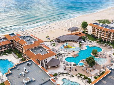 Hotelanlage mit mehreren Pools, Strandzugang und Terrassen mit Sonnenschirmen am Meer.