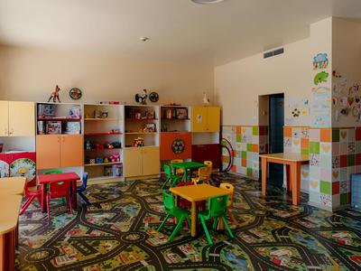 Bunter Kinderspielraum mit kleinen Tischen, Stühlen und Regalen in warmem Licht.