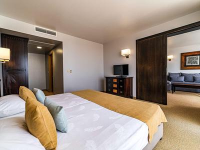 Modern eingerichtetes Hotelzimmer mit Doppelbett, Flachbildfernseher und angrenzendem Sitzbereich.