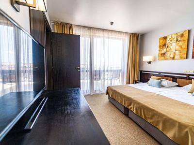 Helles Hotelzimmer mit großem Bett, Schreibtisch und Balkon mit Blick nach draußen.