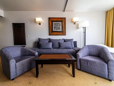 Moderner Hotel- oder Wohnzimmerbereich mit grauen Sesseln, Sofa und Holztisch auf beigem Teppich.