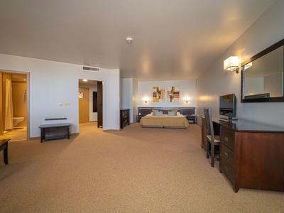 Geräumiges Hotelzimmer mit Doppelbett, Teppichboden, Schreibtisch, Fernseher und Badezimmer im Hintergrund.