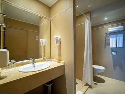 Helles Hotelbadezimmer mit Waschbecken, Spiegel, Haartrockner und Duschkabine.