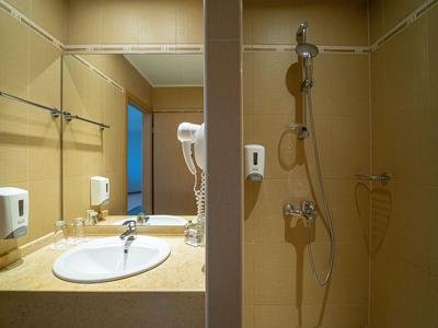 Ein Hotelbadezimmer mit Waschbecken, Spiegel, Haartrockner und begehbarer Dusche in warmen Farben.