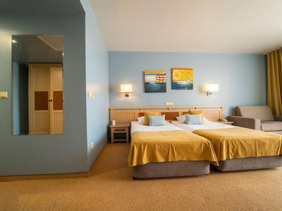 Hell eingerichtetes Hotelzimmer mit zwei Einzelbetten, Kunstwerken und Sofa.