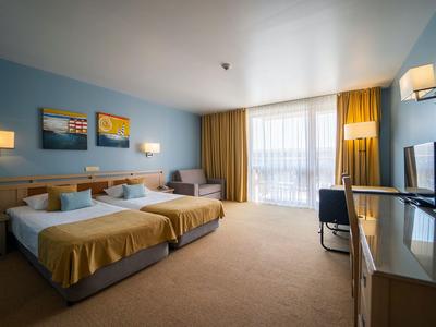 Modern eingerichtetes Hotelzimmer mit zwei Betten, großem Fenster und sonnengelber Dekoration.
