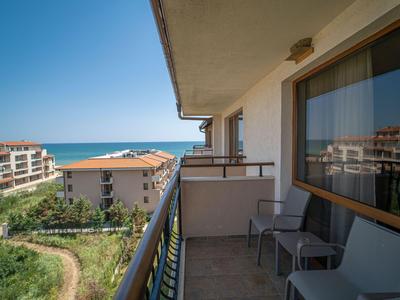 Balkon mit Stühlen und Meerblick in einem Hotel nahe anderer Gebäude und Grünflächen.