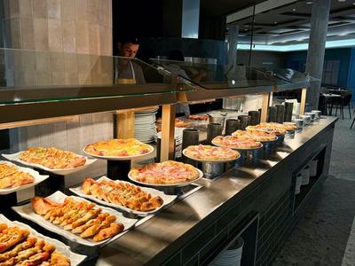 Buffet mit einer Vielzahl von kleinen Gerichten in rechteckigen weißen Tellern auf Edelstahltheke.