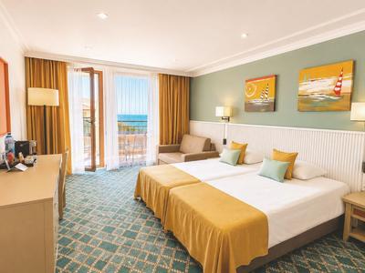 Modernes Hotelzimmer mit Doppelbett, Sofabereich und Blick auf den Balkon zum Meer.