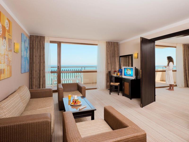 Sala de estar luminosa de una habitación de hotel con vista al mar a través de grandes ventanas y mobiliario moderno.