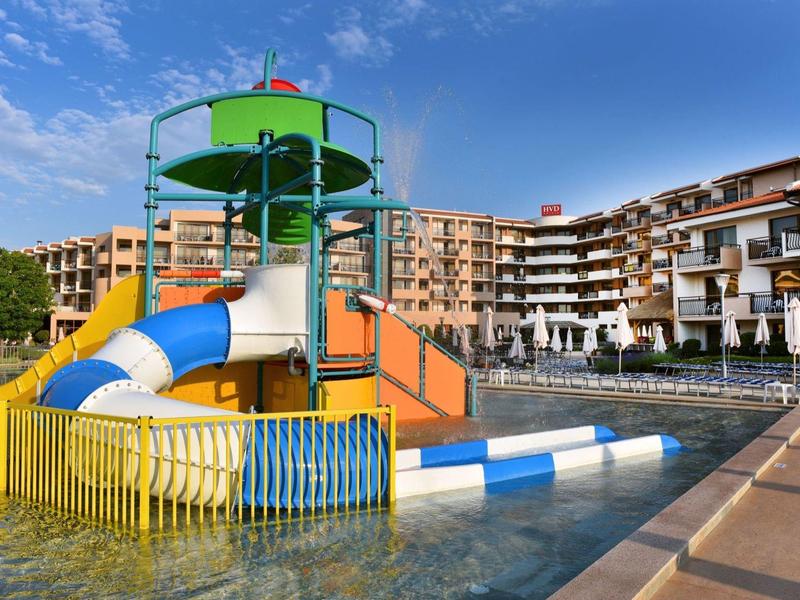 Área de toboganes acuáticos coloridos en una piscina de hotel con edificios de varios pisos al fondo.