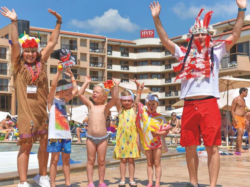 Niños y adultos con tocados juegan y celebran en la piscina de un hotel.