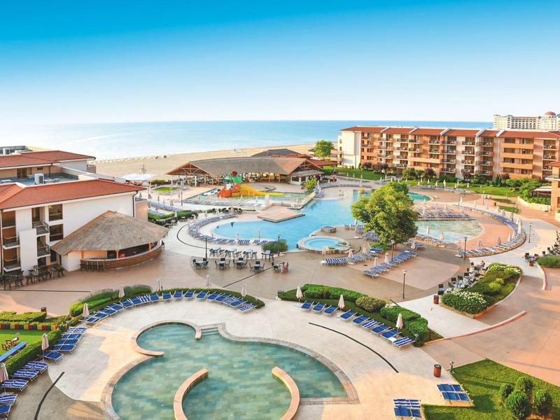 Vista de gran área de piscinas del hotel con varias piscinas, tumbonas y mar al fondo.