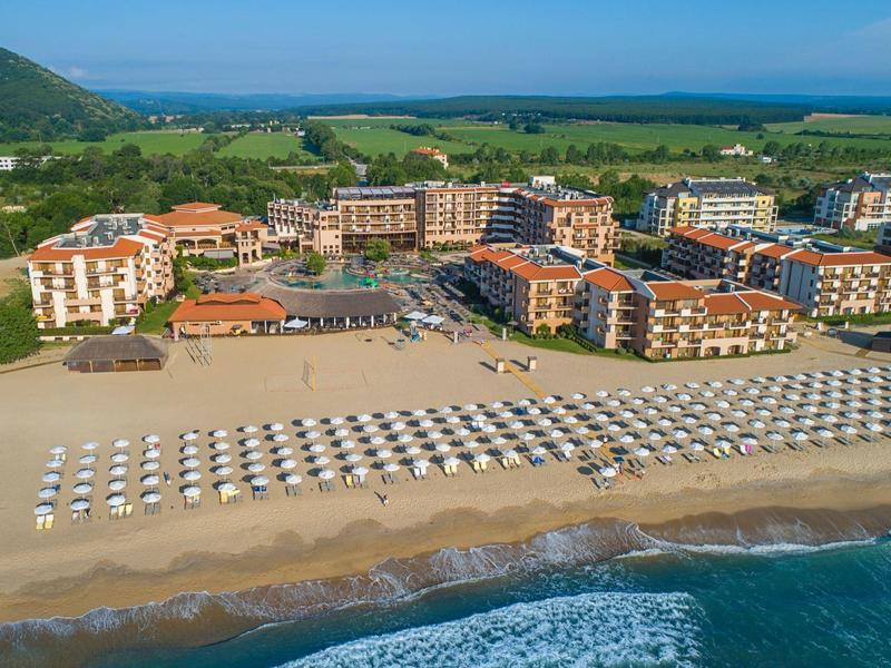 Vista de una playa con filas de sombrillas y un gran complejo hotelero al fondo.