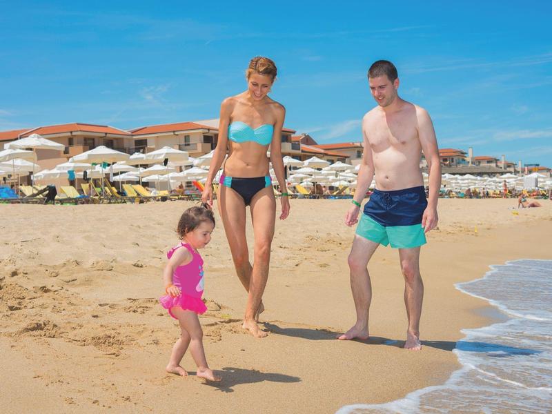 Familia caminando en la playa con arena y mar bajo un cielo azul despejado.