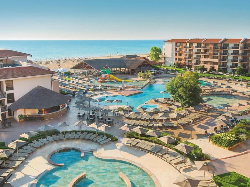 Gran complejo hotelero con varias piscinas, tumbonas y vista al mar bajo cielo despejado.