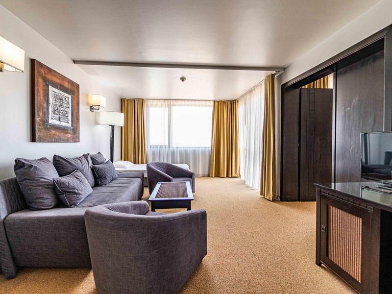 Sala luminosa con sofá gris, sillón y grandes ventanas con cortinas amarillas.