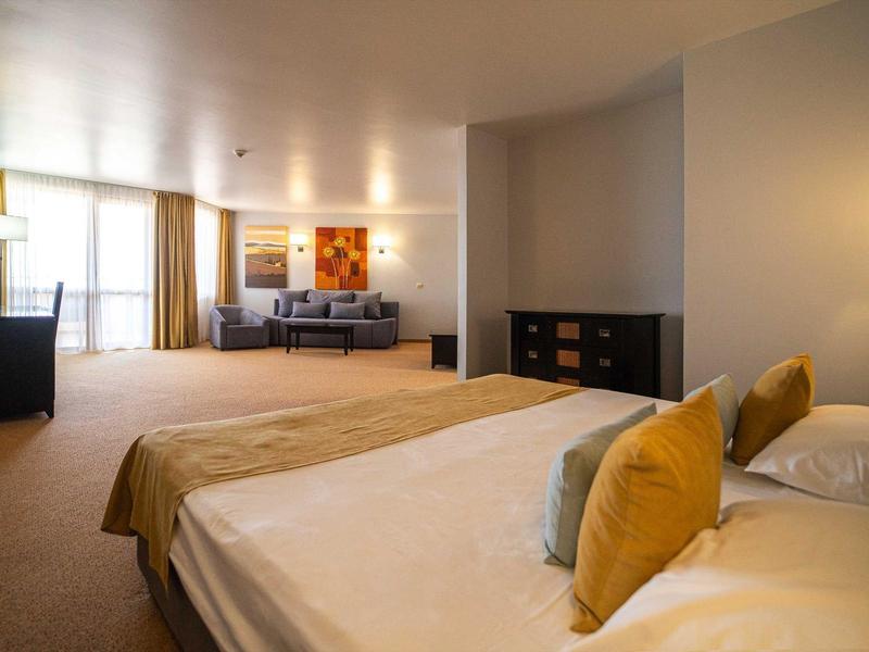 Habitación de hotel grande con cama doble, sofá, escritorio y luz cálida.