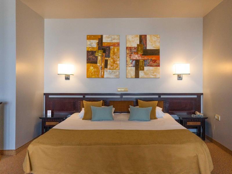 Dormitorio moderno con cama grande, cojines coloridos y cuadros abstractos en la pared.