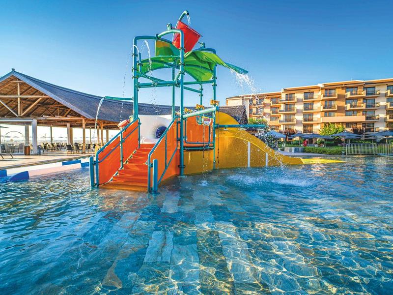 Parque acuático con toboganes y elementos de agua en una piscina de hotel bajo cielo despejado.