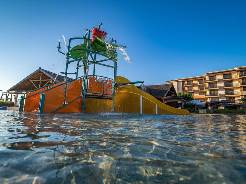 Parque acuático con toboganes y un edificio al fondo bajo un cielo azul claro.