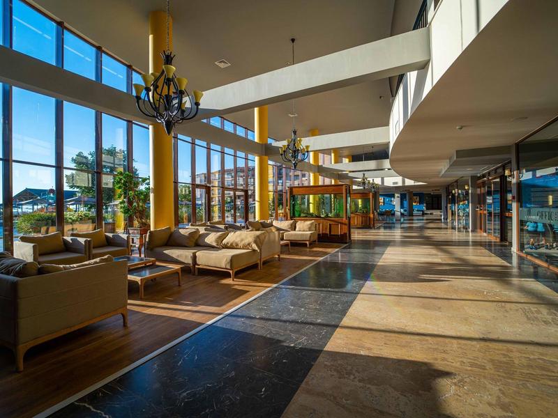 Luminosa recepción de hotel con grandes ventanales, sofás y lámpara moderna a la luz del día.