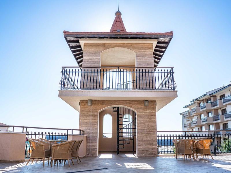 Terraza soleada con torre de observación y muebles exteriores en edificio moderno de hotel.