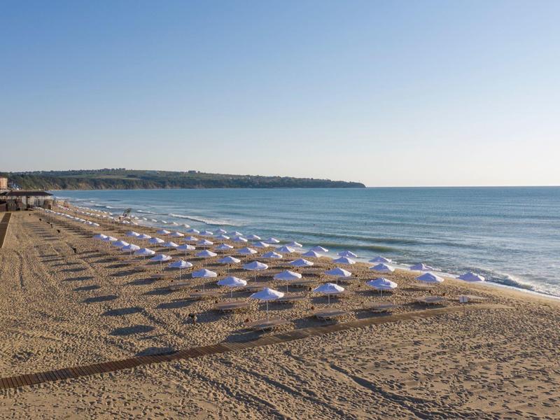 Ancha playa de arena con filas de sombrillas blancas junto a un mar tranquilo bajo un cielo despejado.