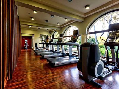 Fitnessraum mit Laufbändern und Crosstrainern vor großen Fensterflächen und Holzboden.