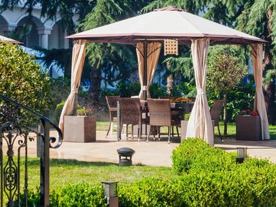 Freistehendes Pavillon mit Stuhl- und Tischgarnitur auf Terrasse in grünem Garten.