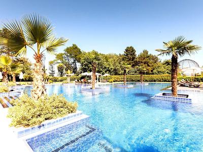 Großer Pool mit blauer Wasserfläche, Palmen und Sonnenschirmen bei klarem Himmel.