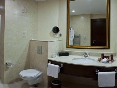 Badezimmer mit beiger Fliese, Dusche, Toilette, Waschbecken, Spiegel und Handtüchern an Haltern.