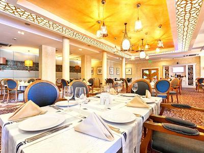 Elegantes Restaurant mit gedeckten Tischen, blauen Stühlen und warmem, hellem Licht.