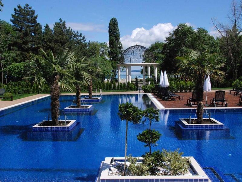 Ein blauer Pool mit Inseln aus Palmen und Pflanzen, umgeben von Bäumen und einer Brücke im Hintergrund.