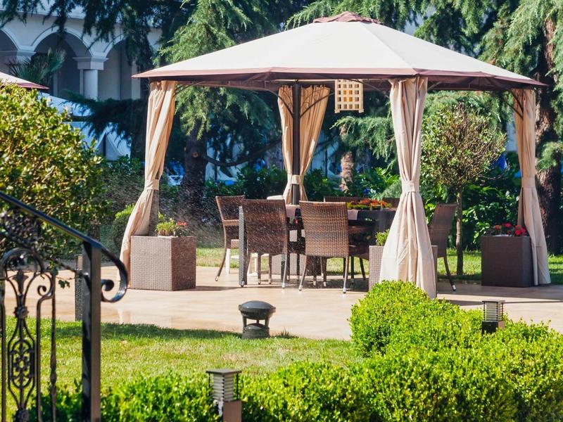 Freistehendes Pavillon mit Stuhl- und Tischgarnitur auf Terrasse in grünem Garten.