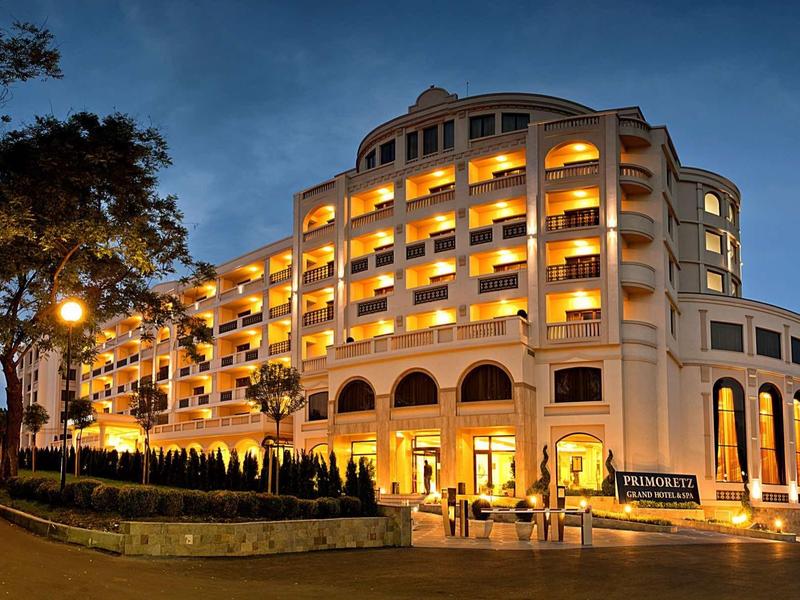 Beleuchtetes großes Hotelgebäude mit Bögen und Balkonen bei Abenddämmerung.