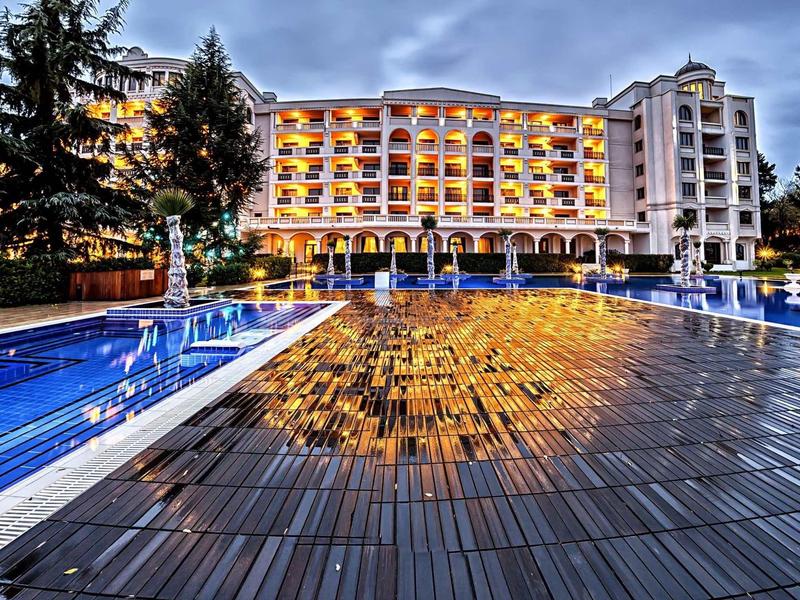 Großes Hotelgebäude mit beleuchteten Balkonen und umgeben von beleuchtetem Pool bei Dämmerung.