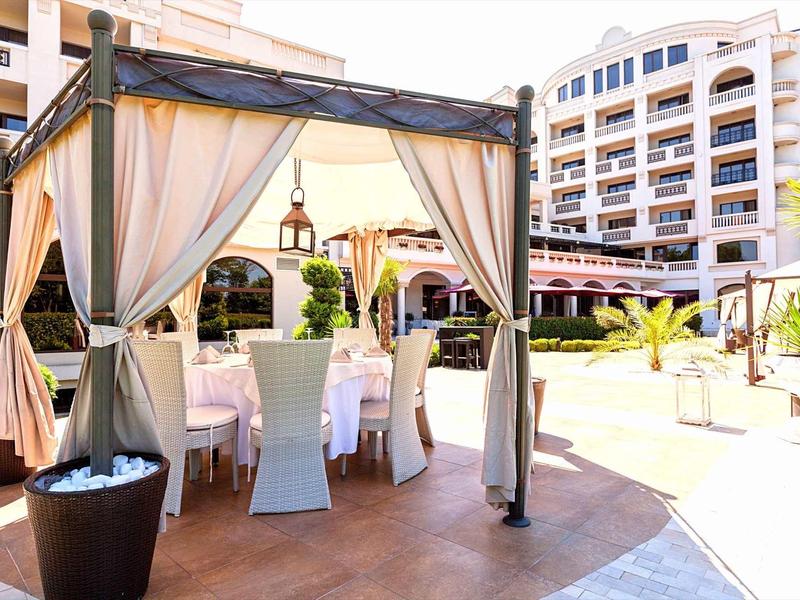 Freiluft-Terrasse mit weißem Pavillon, Tischen, Stühlen und modernen Gebäuden im Hintergrund.