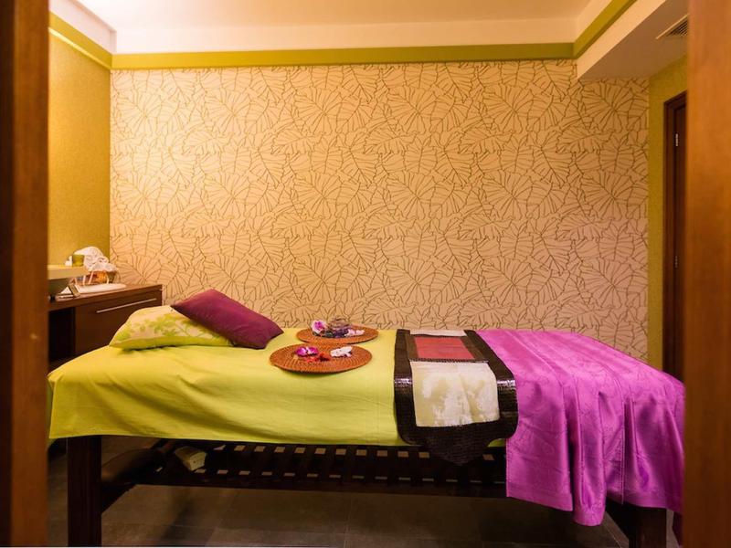 Ein Raum mit einer Massageliege, grünem Laken und lila Decke, dekoriert mit Kissen und Schalen.