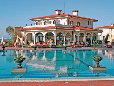 Luxuriöses Hotel mit rotem Dach und großer Poolanlage in sonniger Umgebung.