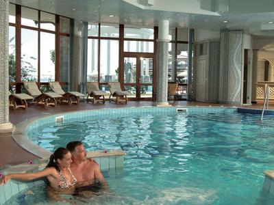 Piscina interior con jacuzzi, sillas reclinables y ventanas grandes que ofrecen luz natural.