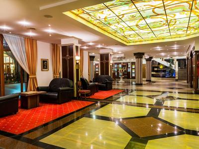 Elegante recepción de hotel con gran vitral en el techo y cómodas áreas de descanso sobre alfombra roja.