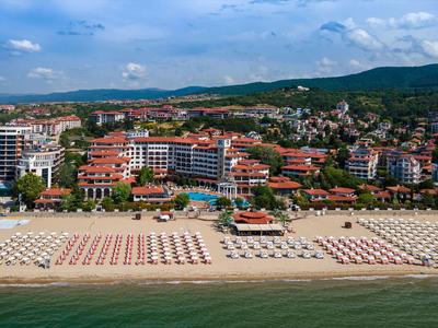 Amplia playa de arena con muchas sombrillas frente a un pueblo costero y colinas boscosas al fondo.